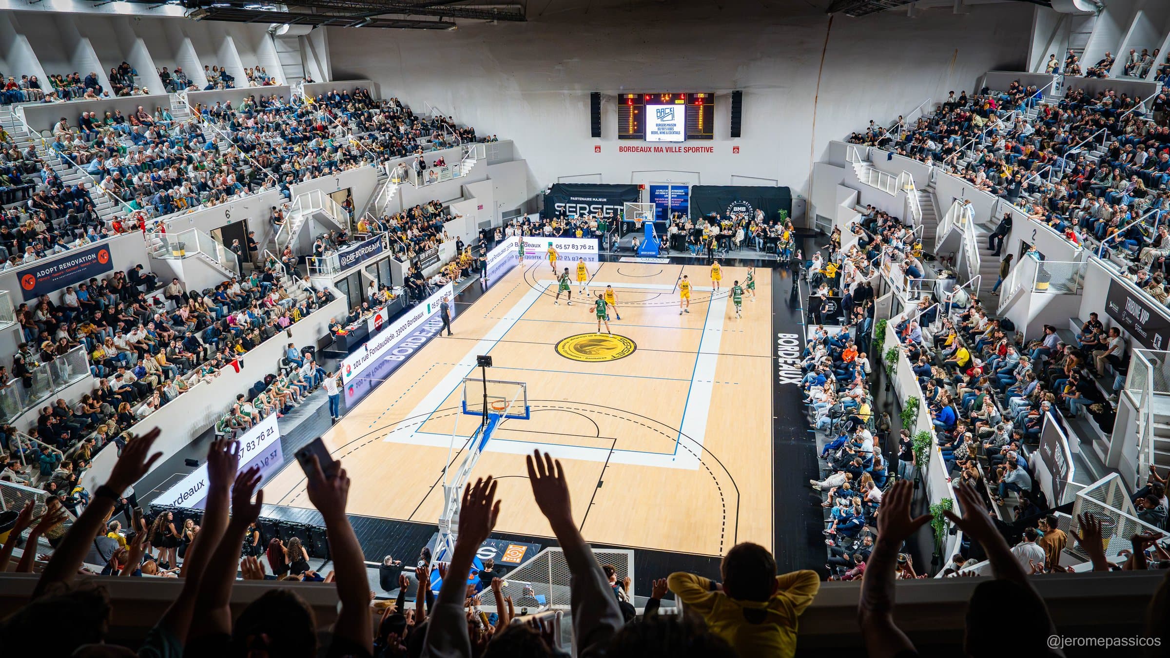 Vue plongeante du Palais des Sports plein, panneaux LED et bâches partenaires autour du parquet